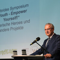 Innen- und Integrationsminister Joachim Herrmann hinter Rednerpult vor Präsentationsleinwand